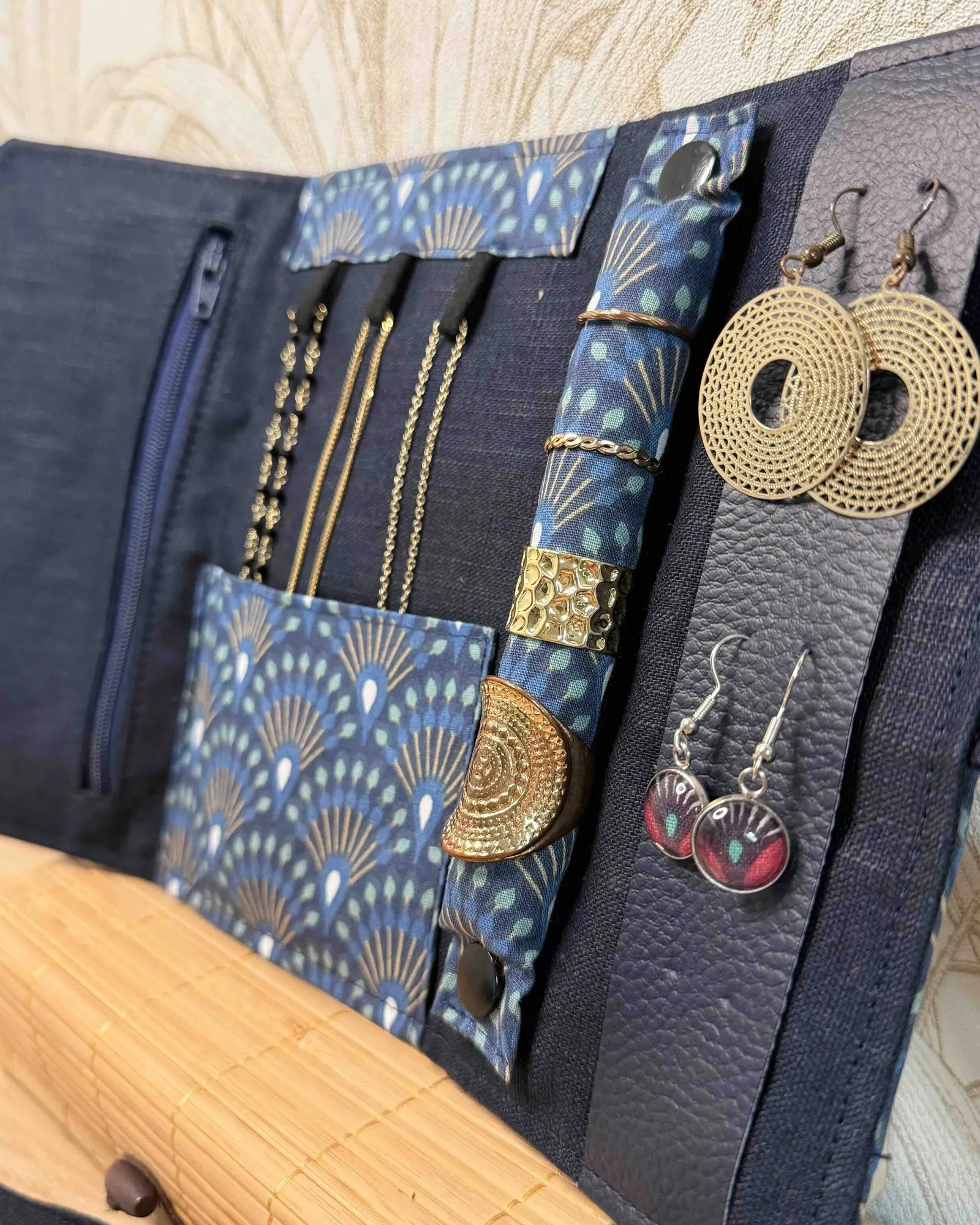 Pochette à bijoux de voyage cousue main, ouverte : colliers accrochés, bagues et boucles d’oreilles rangés séparément